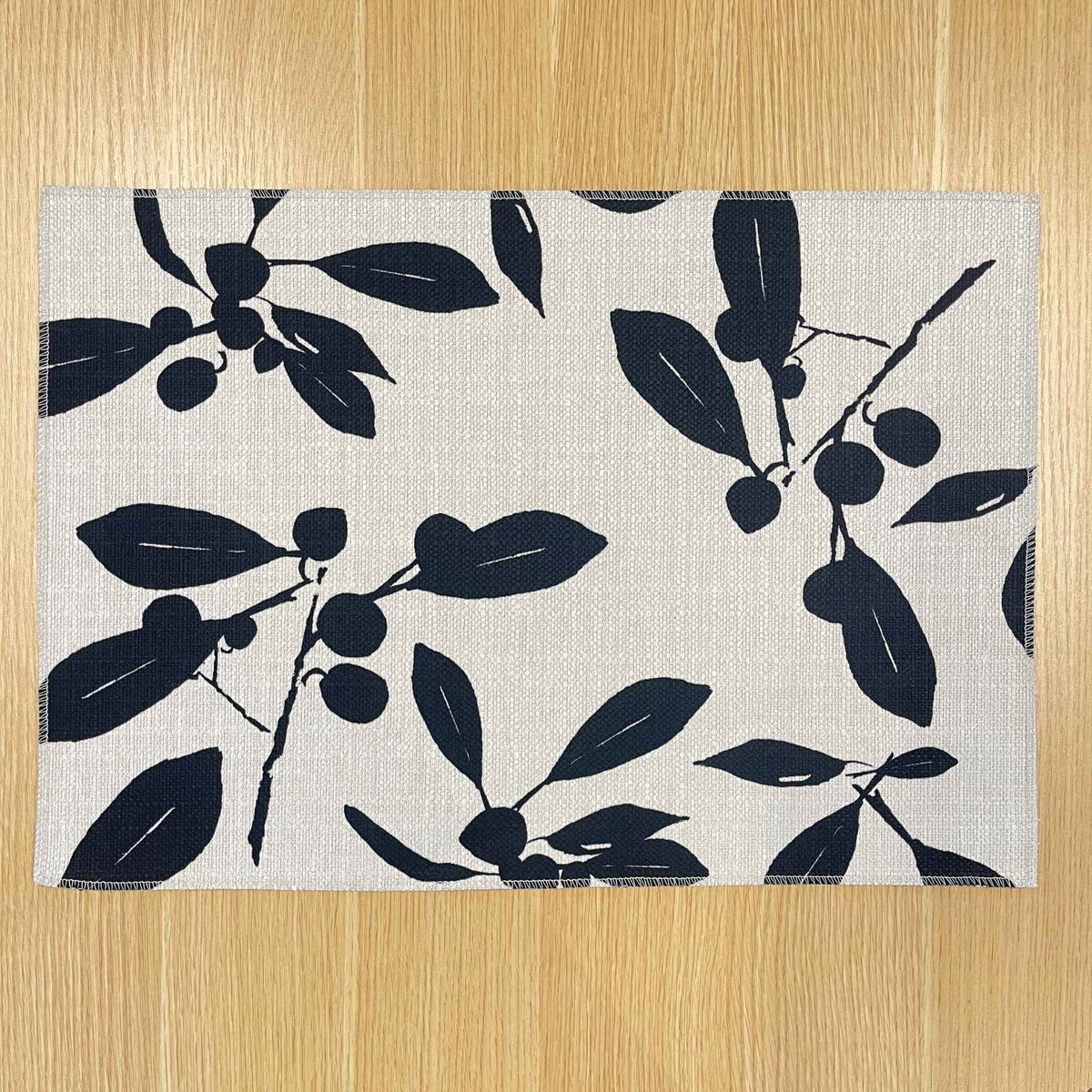 Rectangular Quandong placemat with dark leaf and fruit silhouettes on a pale background, on a wooden tabletop.