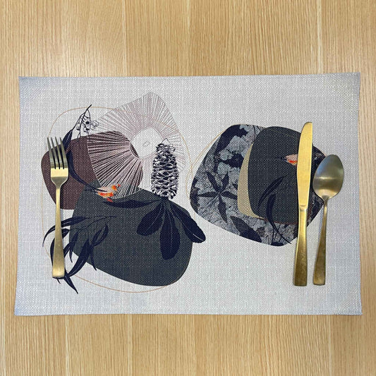 Rectangular Geo Finch placemat with orange-accented finches among black organic shapes and fine geometric lines, on a wooden tabletop with gold cutlery.