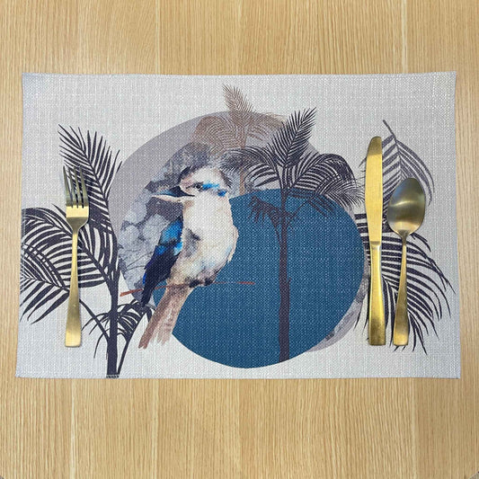 Rectangular Kookaburra placemat with a kookaburra, black palm fronds and a large blue circle, on a wooden tabletop with gold cutlery.