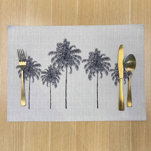 Rectangular Palm Grove placemat with black palm trees on a pale background, on a wooden tabletop with gold cutlery.