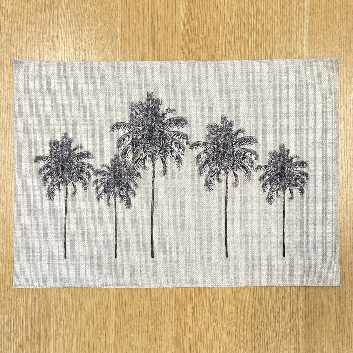 Rectangular Palm Grove placemat with black palm trees on a pale background, on a wooden tabletop.