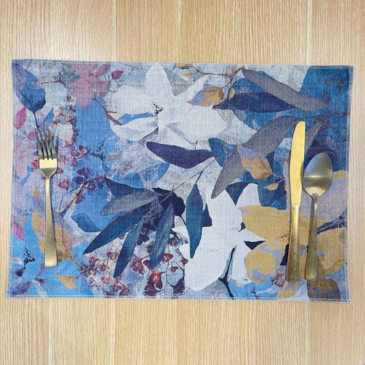 Rectangular Magnolia placemat with layered blue, lavender and white magnolia flowers with ochre accents, on a wooden tabletop with gold cutlery.