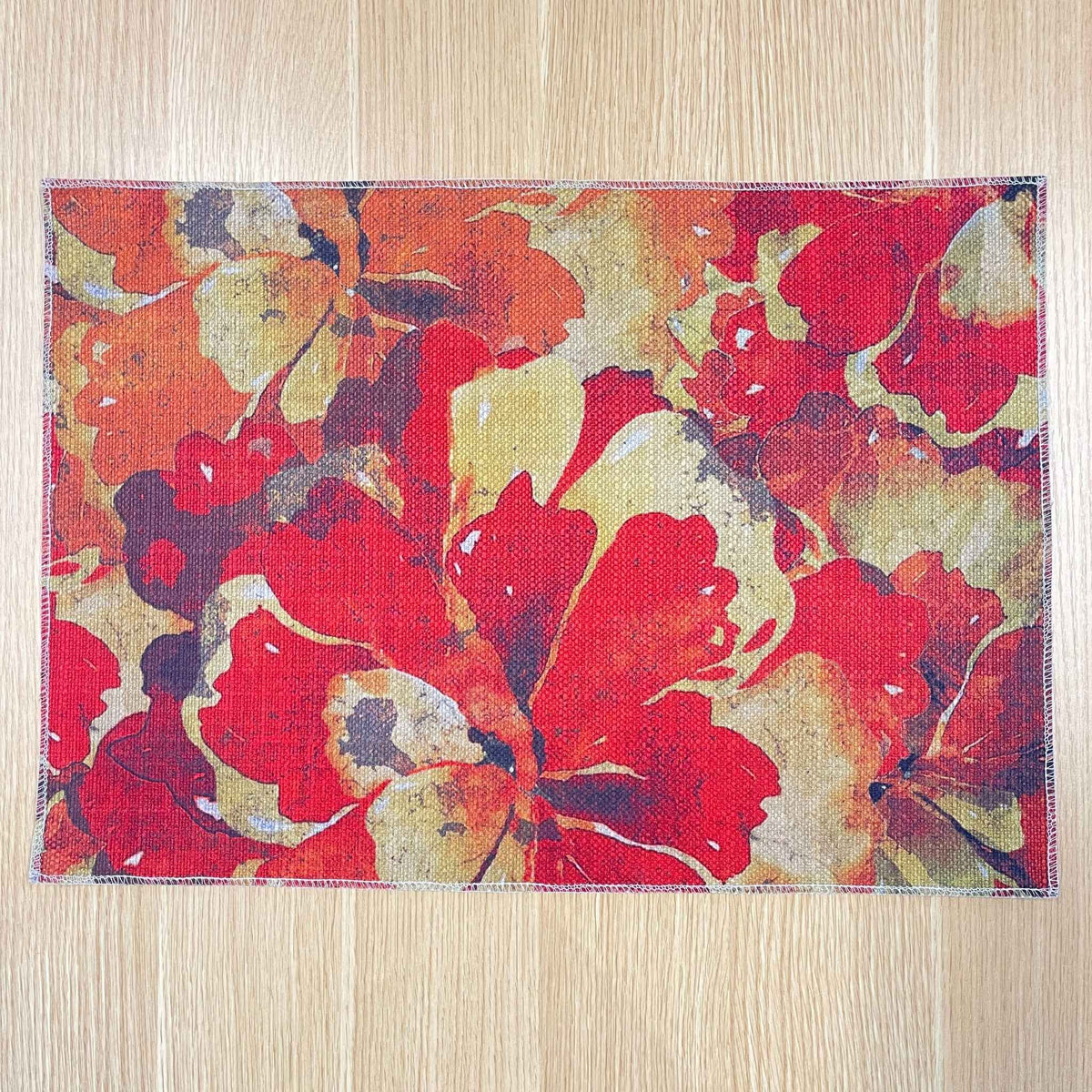 Rectangular Marigold Detail placemat with layered red, orange and gold flowers, on a wooden tabletop.