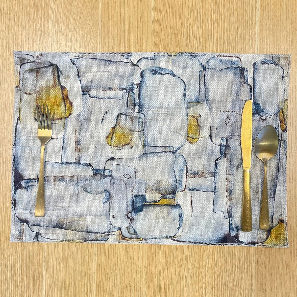 Rectangular Mid Century placemat with abstract grey and blue shapes with ochre accents, on a wooden tabletop.