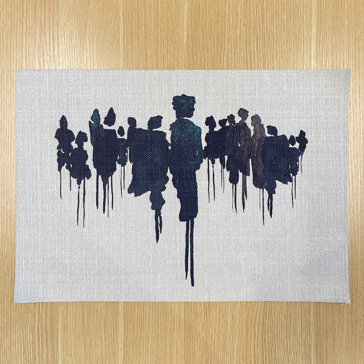 Rectangular Migration placemat with dark abstract silhouettes on a pale background, on a wooden tabletop.