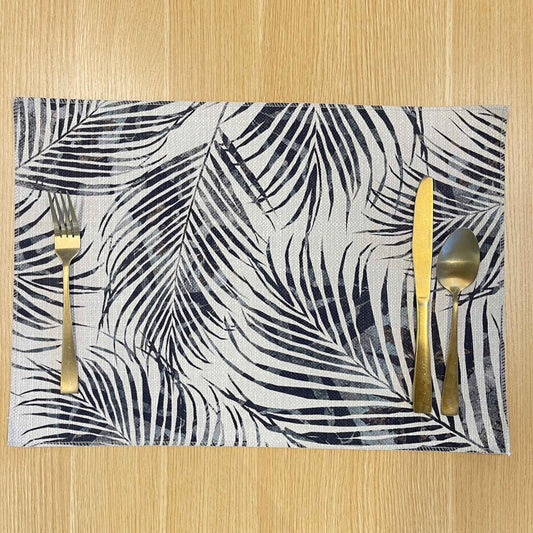 Rectangular Palm Frond placemat with overlapping black and grey palm fronds, on a wooden tabletop with gold cutlery.
