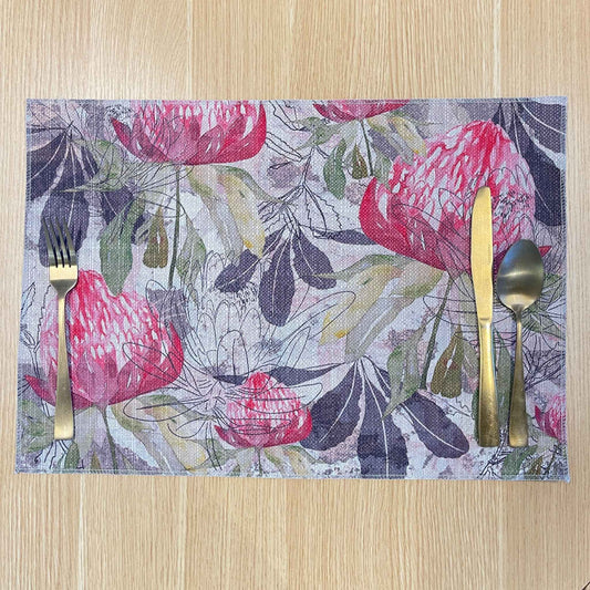 Rectangular Pink Australiana placemat with pink protea flowers among green and grey foliage, on a wooden tabletop.