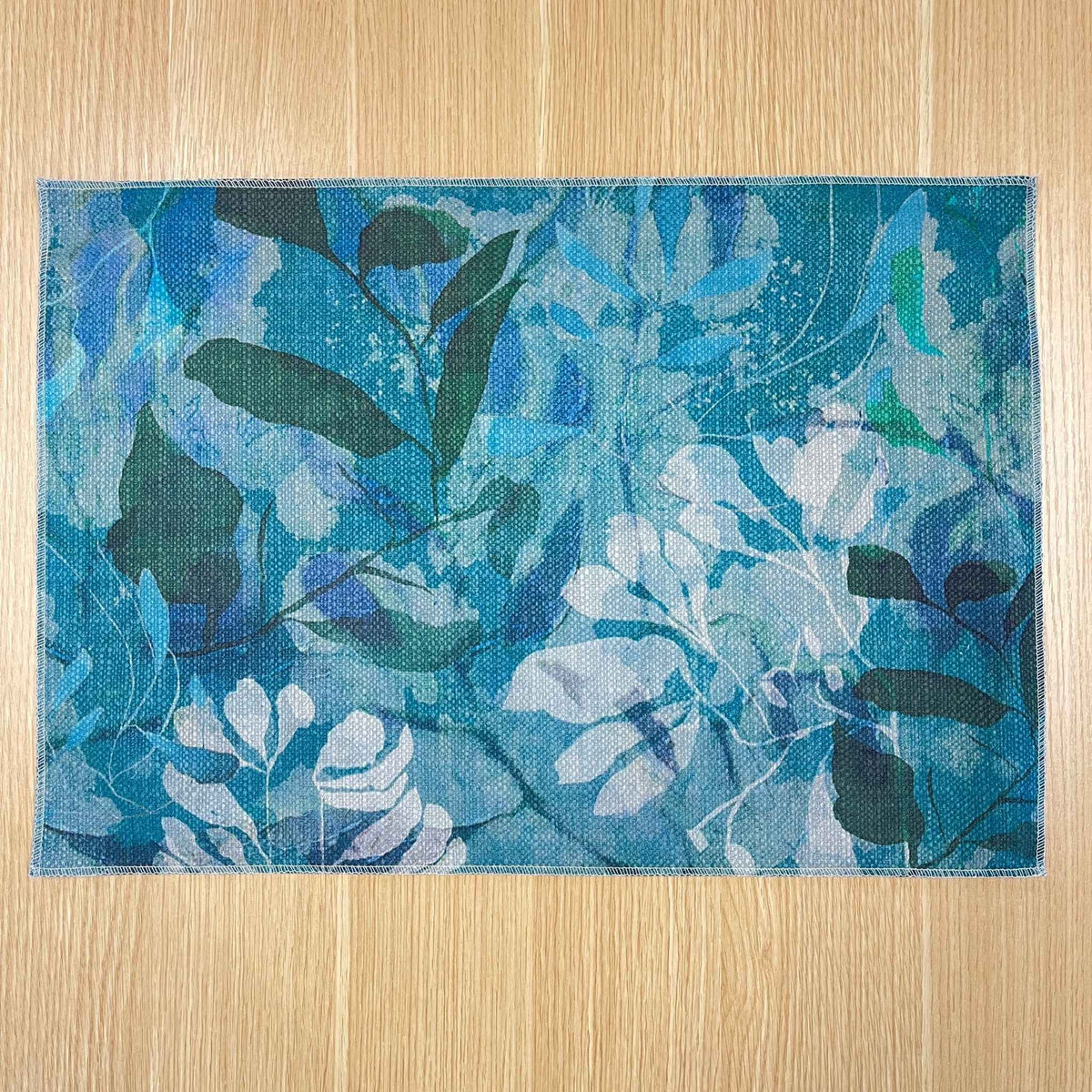 Rectangular Rock Pool placemat with layered turquoise, blue and green foliage, on a wooden tabletop.