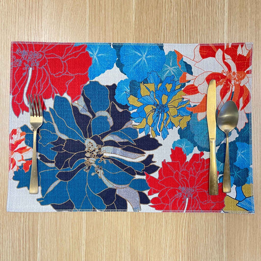 Rectangular Sunset placemat with large blue, red and yellow flowers on a pale background, on a wooden tabletop with gold cutlery.