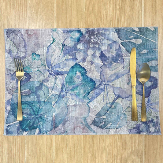 Rectangular Wild Garden placemat with layered blue, lavender and teal botanical shapes, on a wooden tabletop with gold cutlery.