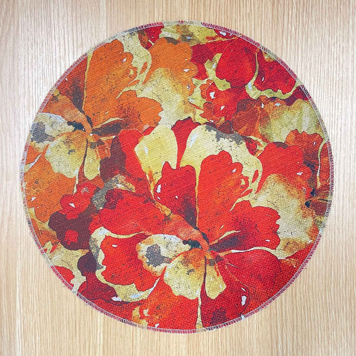 Round Marigold Detail placemat with layered red, orange and gold flowers, on a wooden tabletop.