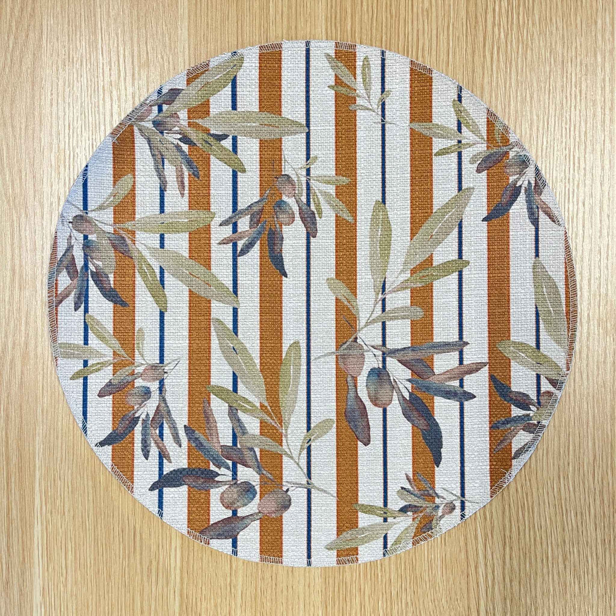 Round Olive and Sol placemat with olive branches over terracotta and navy stripes, on a wooden tabletop.