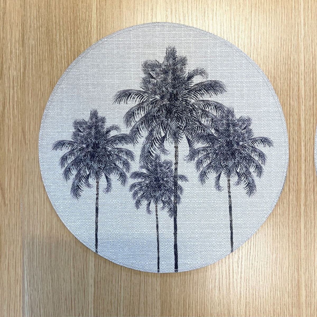 Round Palm Grove placemat with black palm trees on a pale background, on a wooden tabletop.
