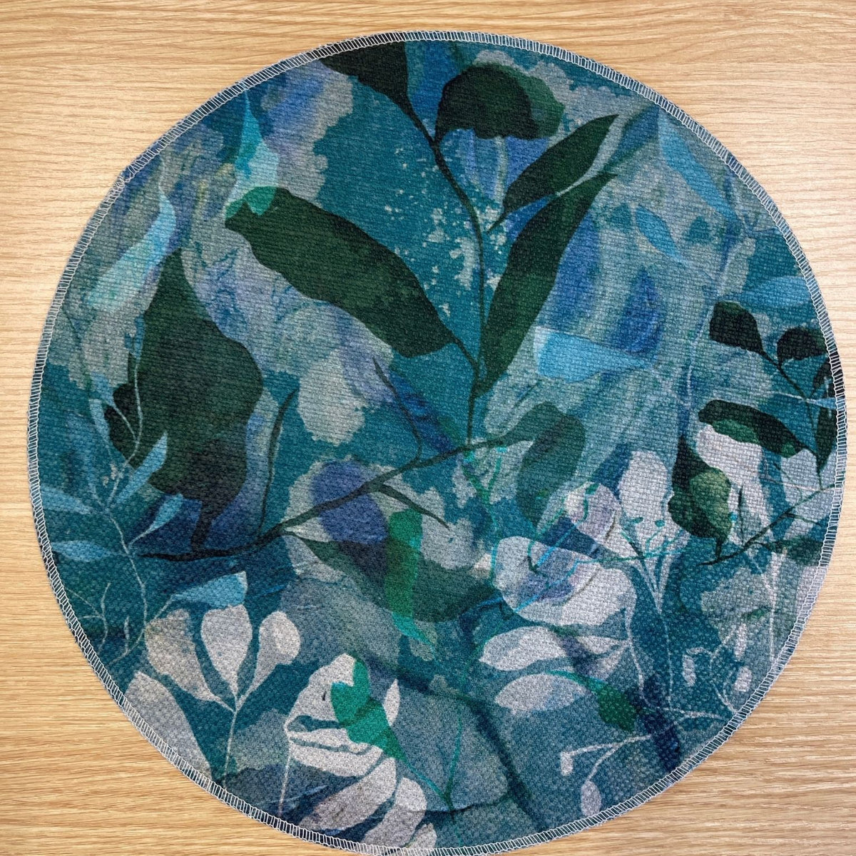 Round Rock Pool placemat with layered turquoise, blue and green foliage, on a wooden tabletop.