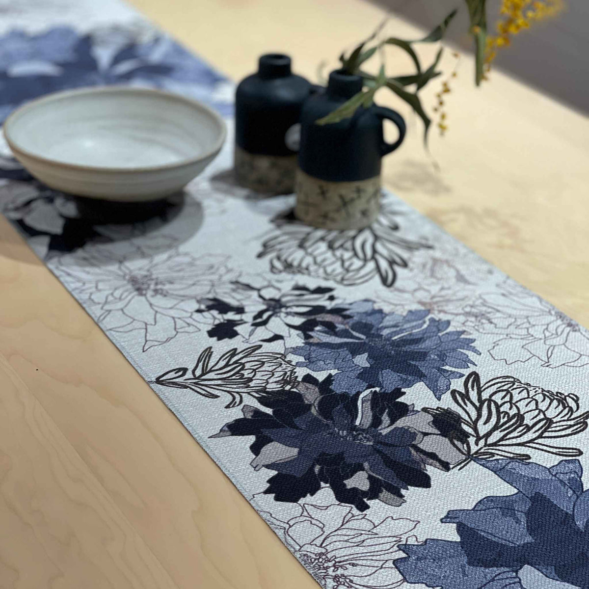 Image 2
Antique Floral Blue table runner with navy and blue flowers with fine floral outlines on a pale background, styled with a ceramic bowl and dark jug.